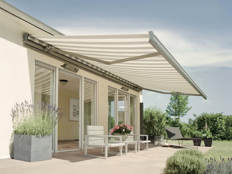 Une maison avec une terrasse, une marquise rayée, des pots de fleurs et une verdure environnante.