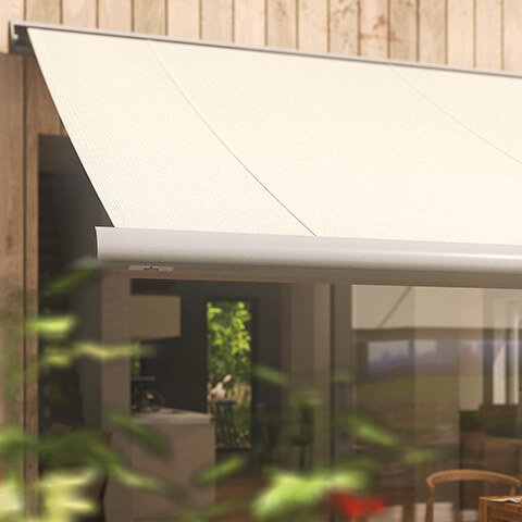 Marquise beige installée sur une façade en bois, avec un fond flou d'une terrasse et d'un espace intérieur.
