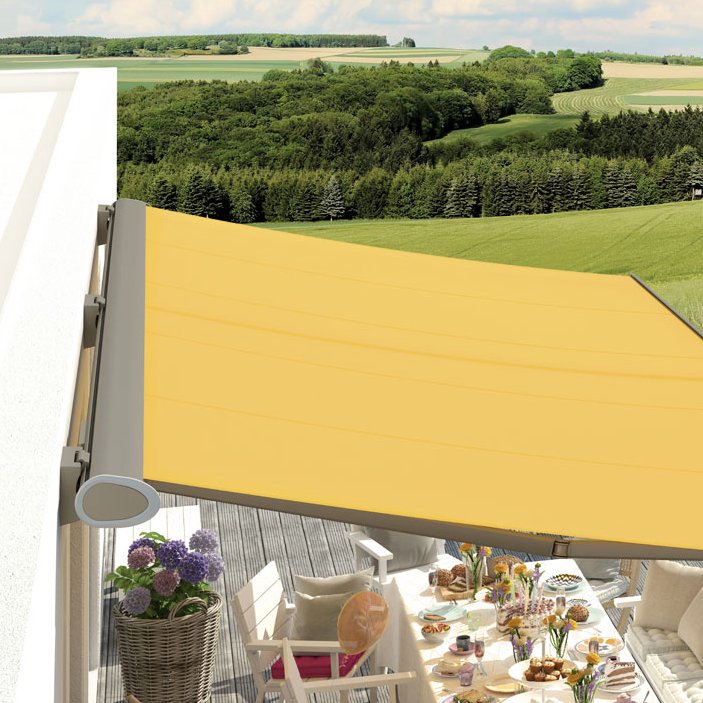 Un espace terrasse avec une grand table et une marquise jaune, entouré de verdure.