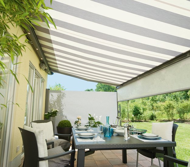 représentation d'une terrasse avec une toile de marquise rayée en beige et gris. Mobilier de jardin autour d'une table. 