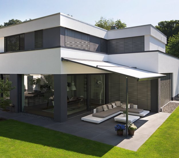 Maison moderne avec un auvent, façades blanches et grises, et une terrasse aménagée. 