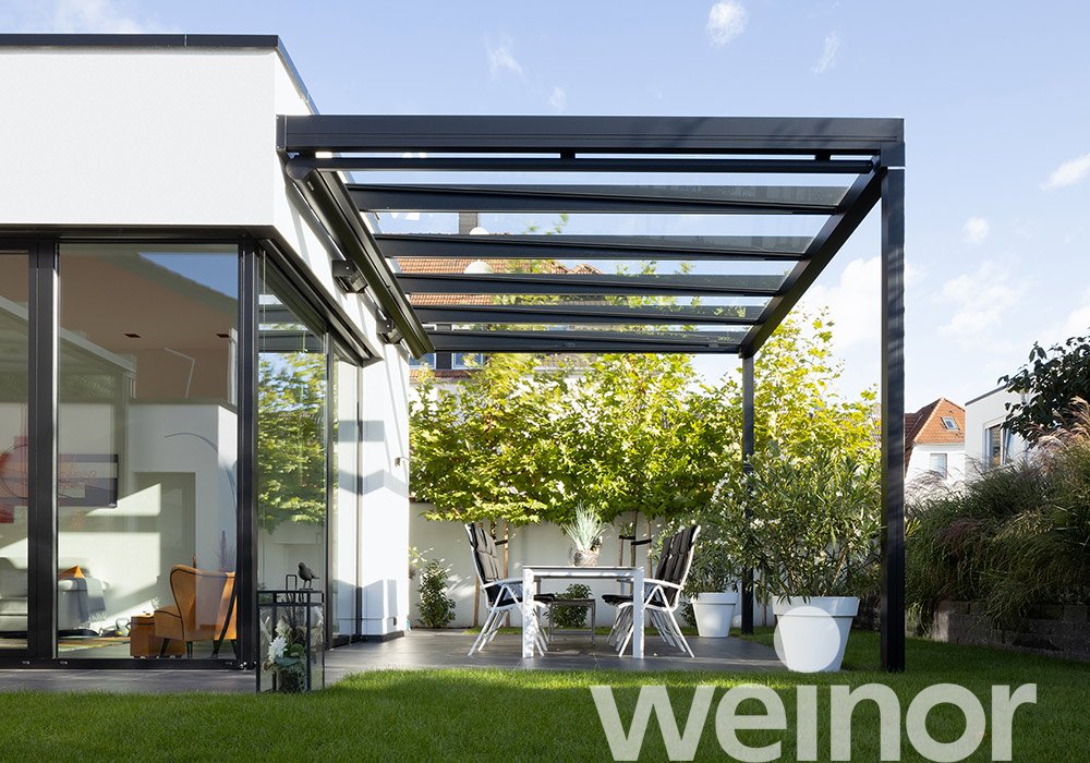 Terrassensituation avec une surdachung noire, des murs en verre et un aménagement verdoyant. 