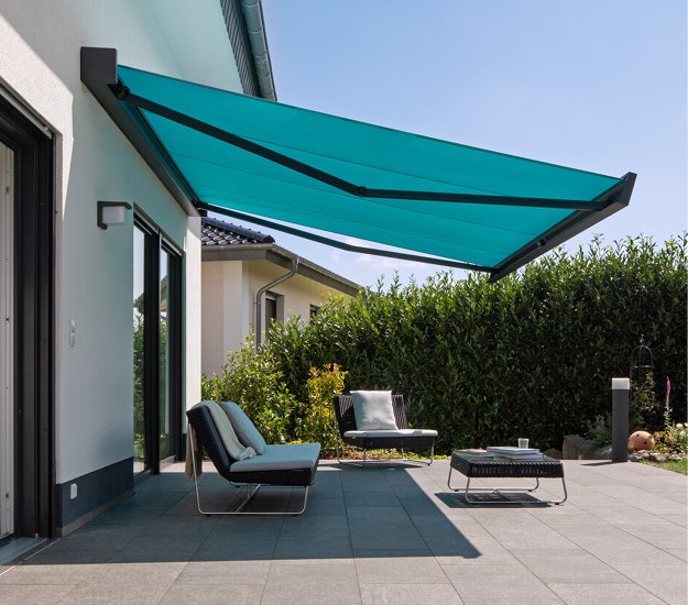 Toit de terrasse en toile turquoise sur une maison, avec des chaises modernes et un jardin en arrière-plan. 