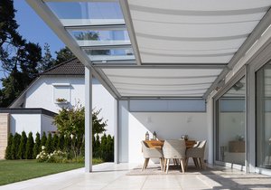 Vue d'une terrasse avec une surdache, mobilier en bois, chaises et verdure en arrière-plan.