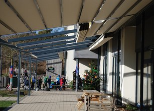 Vue d'un espace extérieur avec des personnes marchant sous des structures de couverture et un arbre de Noël. 