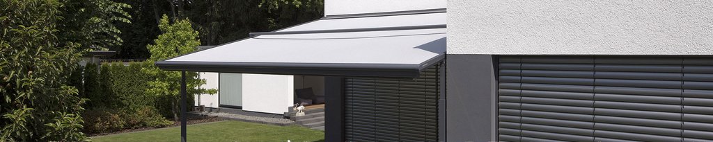 Une marquise grise sur une maison moderne, avec un jardin en arrière-plan.