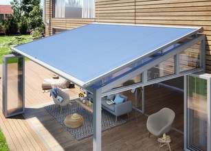 Une surperstructure en verre avec une toiture bleue sur une terrasse en bois, entourée de verdure. 