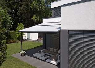 Vue d'une maison moderne avec une marquise blanche sur une terrasse, entourée de verdure. 