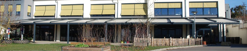 Bâtiment avec auvent et volets jaunes, dominé par des lignes horizontales et un espace extérieur ouvert.