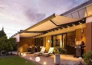 Terrasse élégante avec une grande marquise, éclairage doux et meubles lounge. Atmosphère chaleureuse au coucher du soleil. 