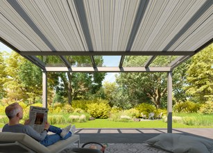 Vue depuis une terrasse couverte avec un homme lisant, entouré d'arbres et de verdure. 