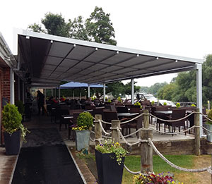 Überdachung mit Markisenkasten über einer Terrassensituation, umgeben von Pflanzen und Möbeln.